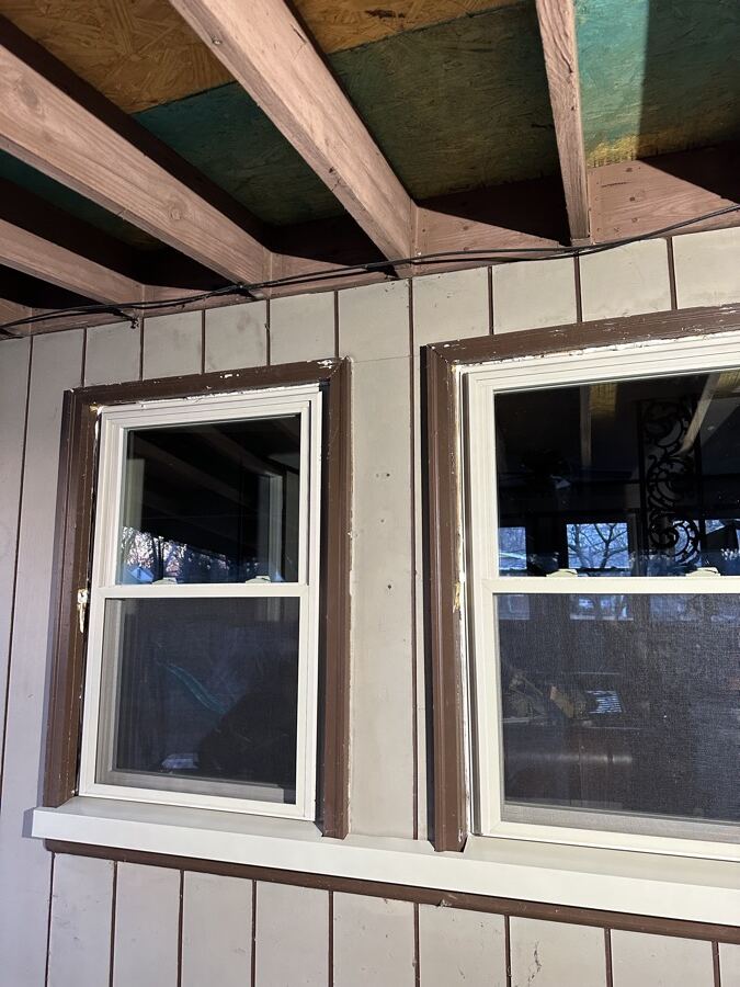Old brown-trimmed windows in an unfinished addition before replacement