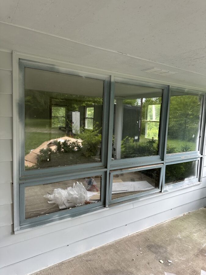 Old dark aluminum triple window on a porch before replacement