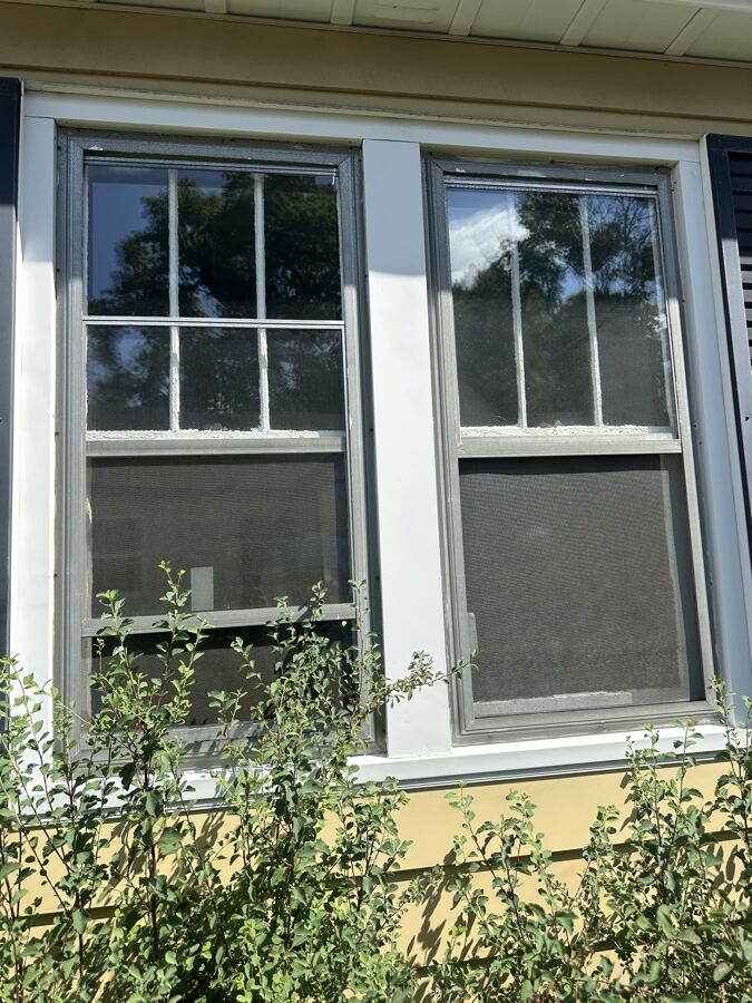Old aluminum double-hung window with worn screens before replacement