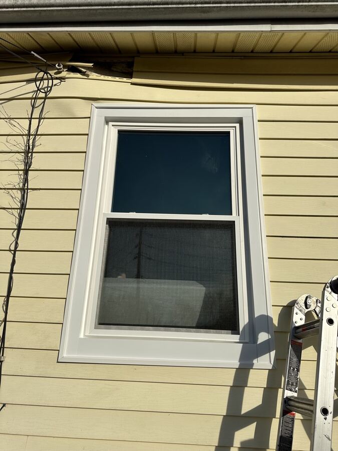 New white window with repaired trim on the same yellow siding after replacement