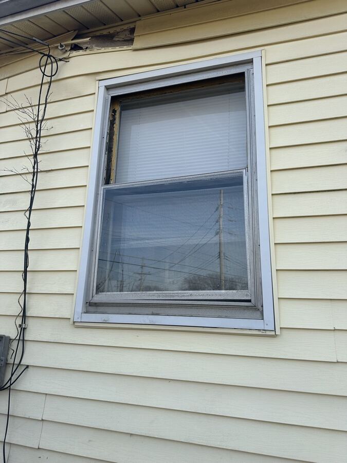 Old aluminum window with damaged trim on yellow siding before replacement